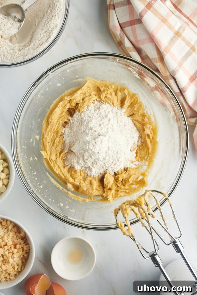 Overhead view of the dry flour mixture being gradually added to the wet ingredients in a mixing bowl, starting to form cookie dough.