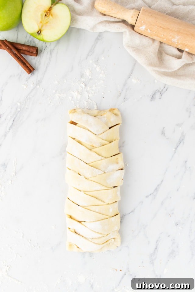 Overhead view of a fully assembled apple strudel, showing the beautiful braided pastry encasing the filling, ready for baking.