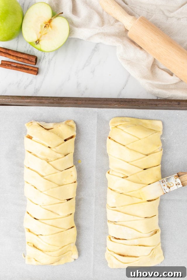Overhead view of an egg wash being delicately brushed onto the assembled apple strudel on a baking sheet, ready for the oven.