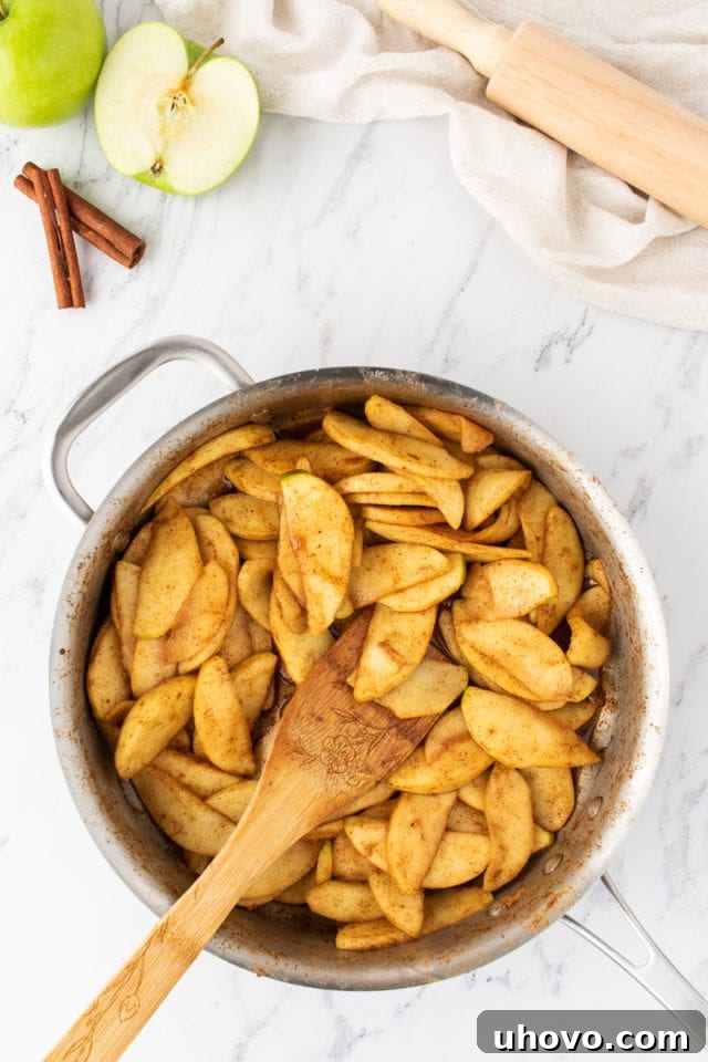 Overhead view of the cooked apple strudel filling, showing softened apples infused with spices and brown sugar, cooling in a saucepan.