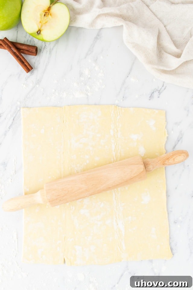 Overhead view of a sheet of rolled puff pastry on a marble surface, gently flattened to smooth out creases.