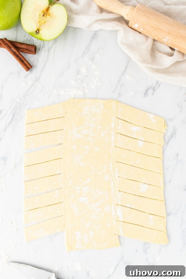 Overhead view of puff pastry meticulously cut with slanted strips on both sides, preparing it for braiding the apple strudel.