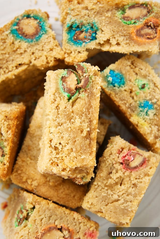 Overhead view of freshly baked Peanut Butter Cookie Bars studded with colorful M&Ms, arranged on a light gray plate, showcasing their inviting texture and generous toppings.