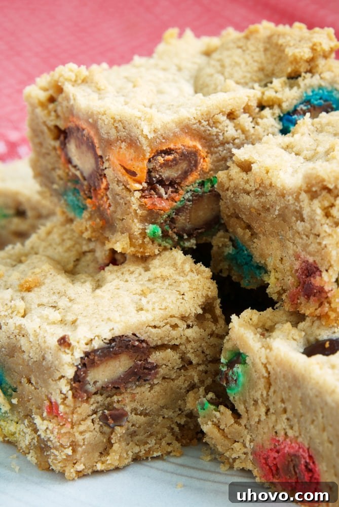 A close-up stack of three homemade Peanut Butter Cookie Bars, revealing their soft, chewy interior and the vibrant M&Ms baked into them, ready to be enjoyed.