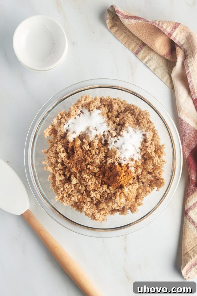 Overhead view of ingredients for breadcrumb topping (toasted crumbs, butter, sugar, spices) in a glass bowl.