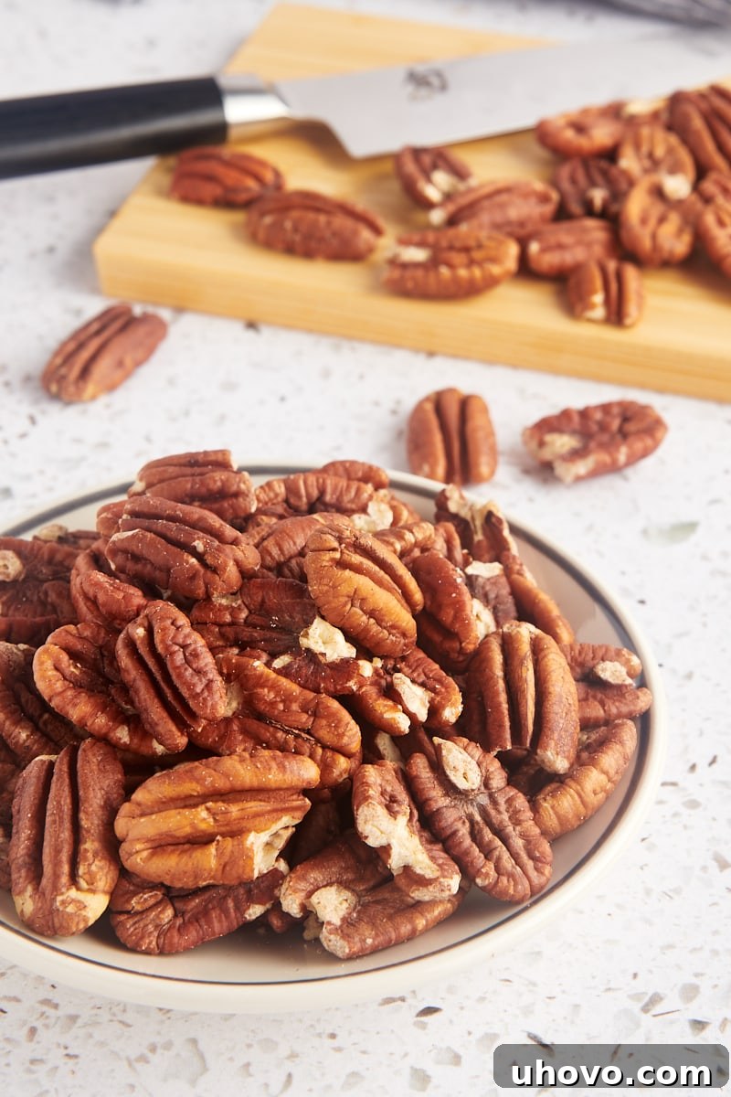 a bowl of toasted pecans with more pecans on a cutting board in the background