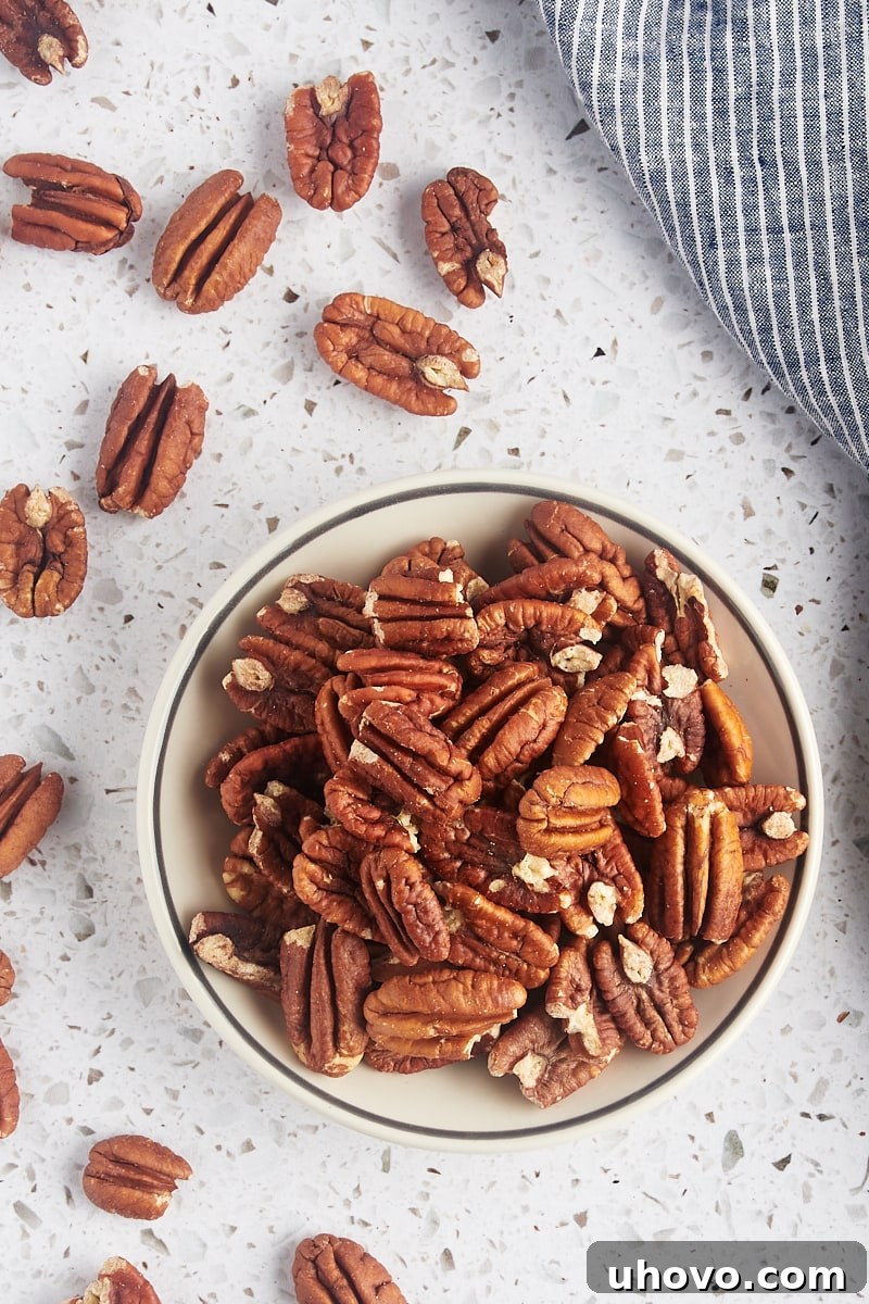 overhead view of toasted pecans in a shallow bowl with more pecans scattered around them