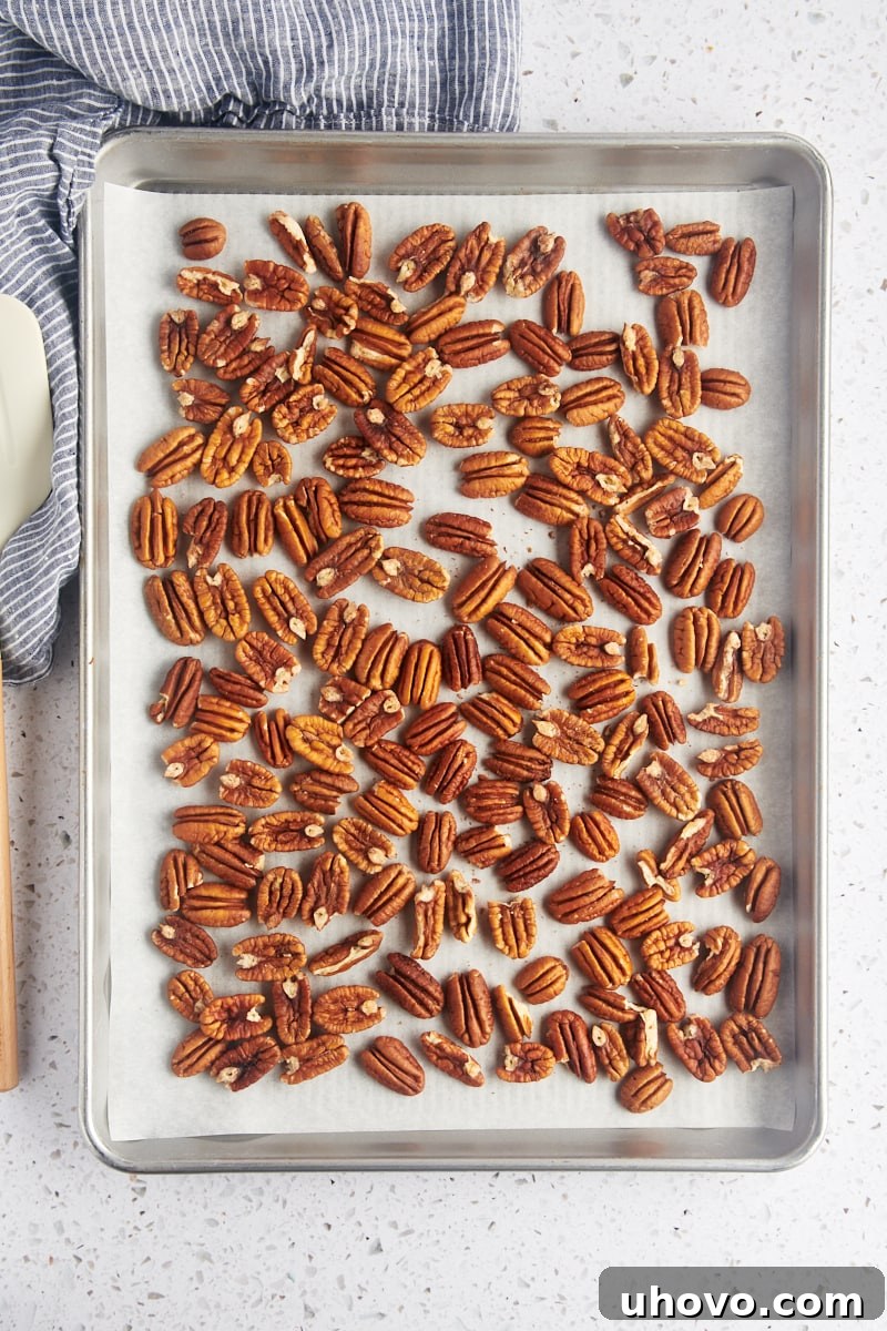 overhead view of pecan halves spread on a parchment-lined baking sheet