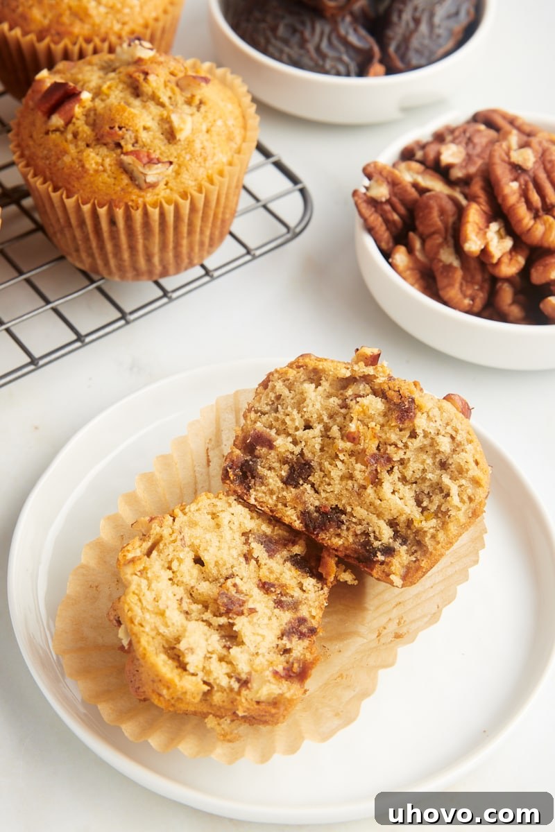 a date nut muffin split in half on a white plate with more muffins in the background