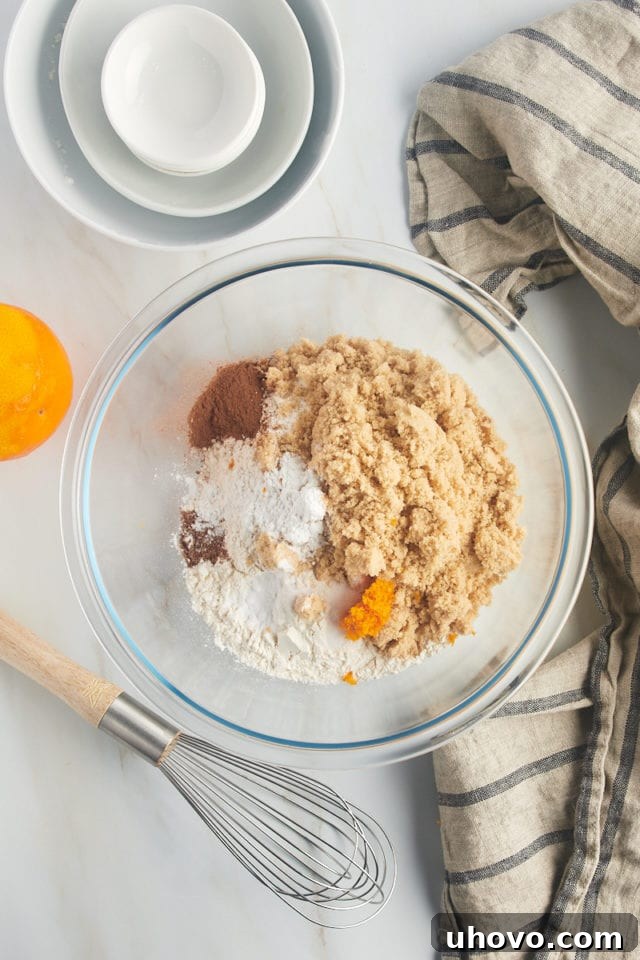 overhead view of flour, brown sugar, baking powder, baking soda, salt, cinnamon, nutmeg, and orange zest in a glass mixing bowl