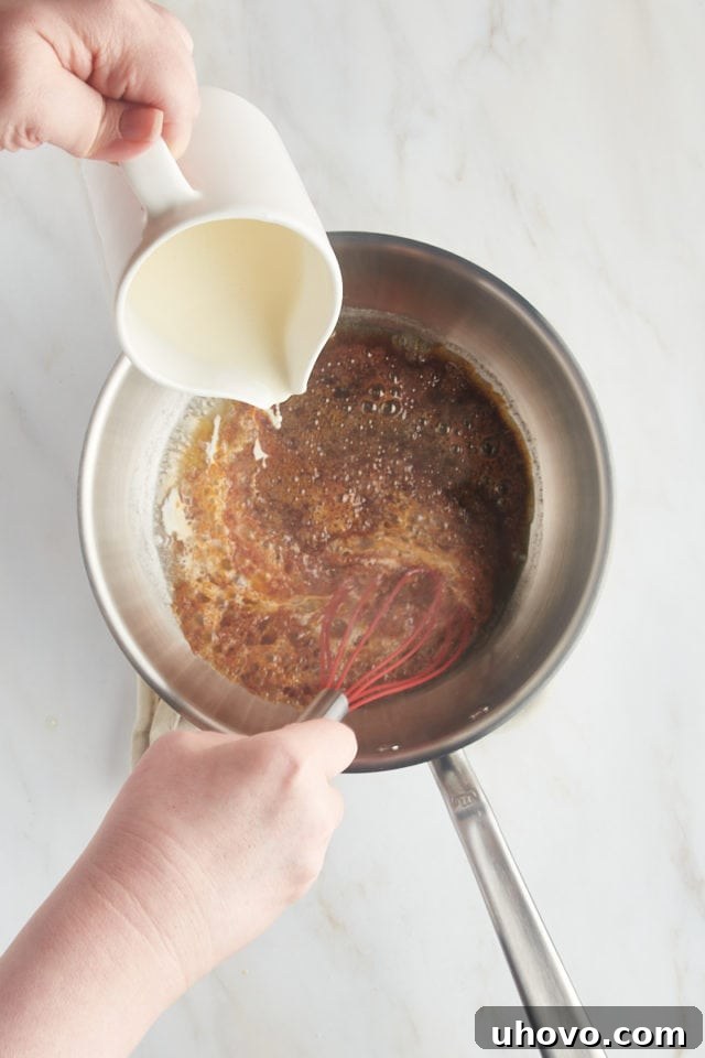 Overhead view of heavy cream being slowly and carefully poured into the hot caramelized sugar, creating a frothy reaction.
