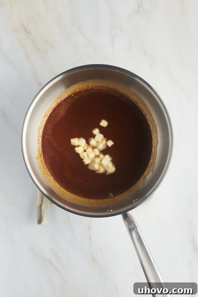 Overhead view of small pieces of butter being added to the warm caramel sauce in a saucepan.