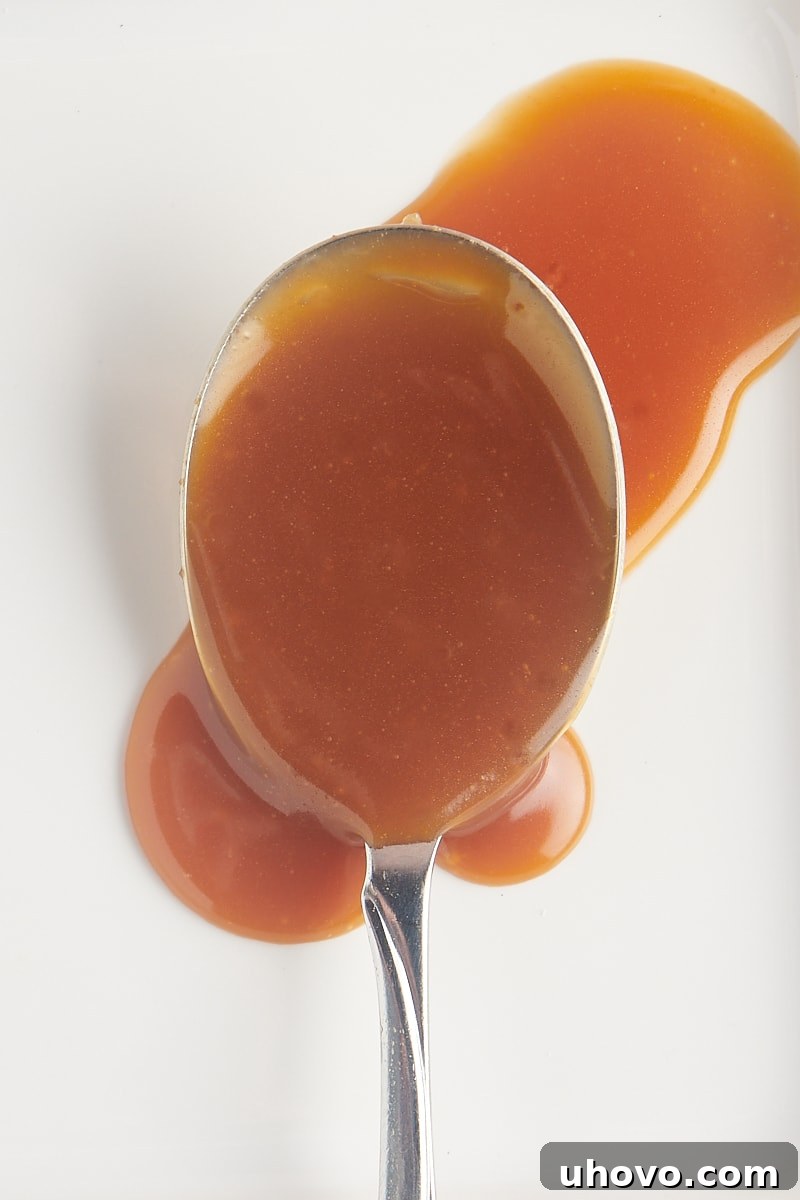 A close-up shot of a spoonful of glossy caramel sauce resting on a white plate, highlighting its smooth texture.