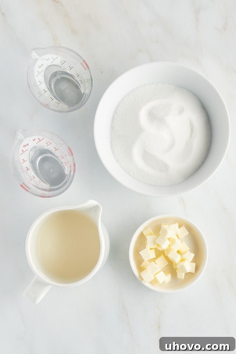 An overhead view of the essential ingredients for caramel sauce laid out: granulated sugar, water, light corn syrup, heavy cream, and butter cubes.