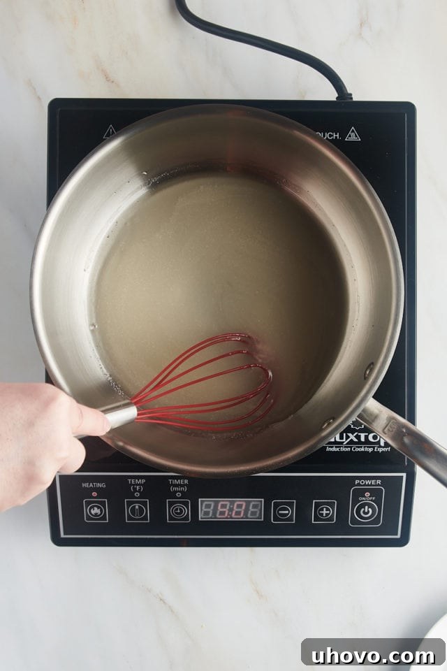 Overhead view of the combined sugar, water, and corn syrup gently heating in a saucepan, beginning to dissolve.