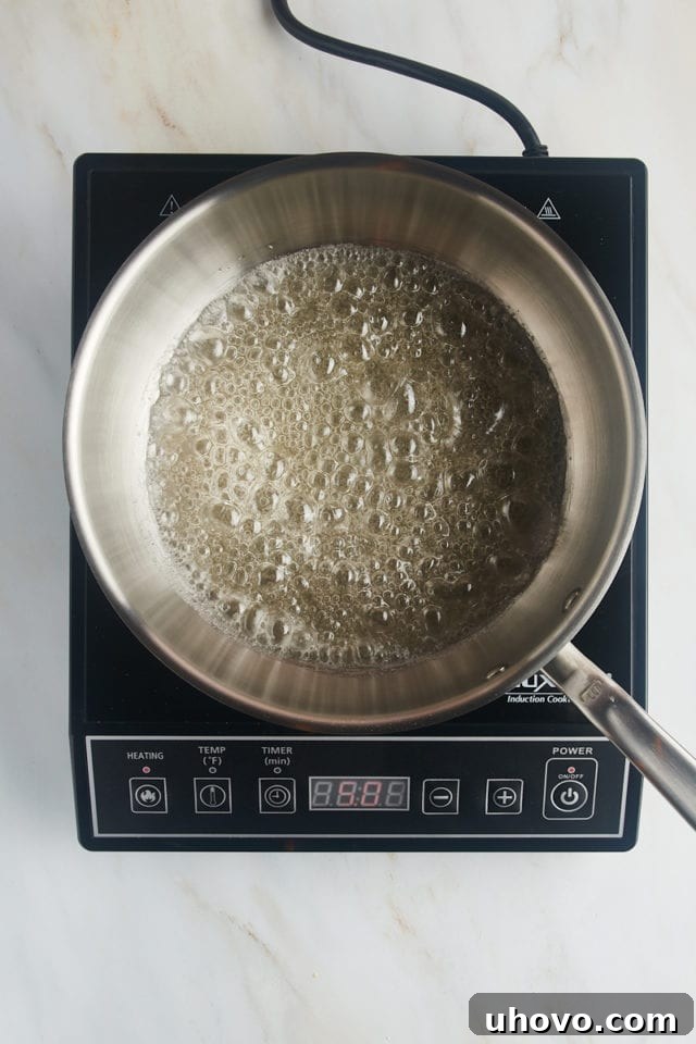 Overhead view of the sugar, water, and corn syrup mixture boiling vigorously in a saucepan, beginning to thicken.