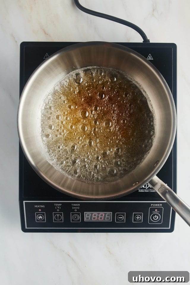Overhead view of amber-colored caramel actively cooking in a saucepan, reaching the perfect shade.