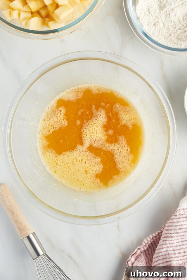 An overhead view captures the moment dark rum and vanilla extract are gently poured into a glass bowl containing the sugar-egg mixture, adding depth of flavor to the French apple cake batter.