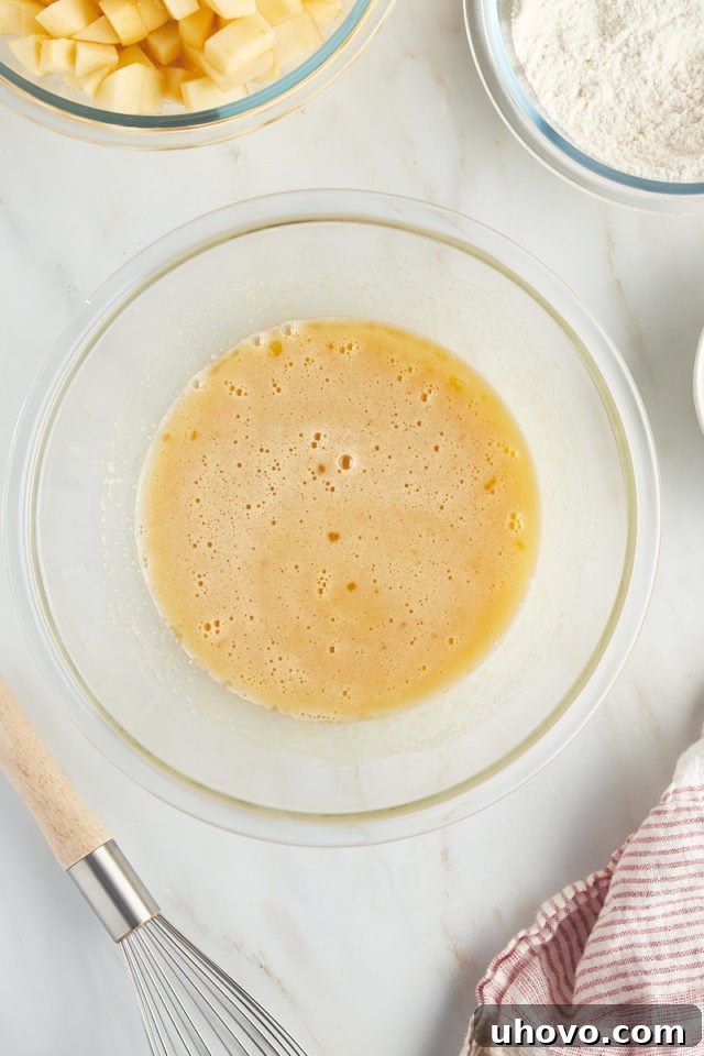 A vibrant overhead shot of the thoroughly mixed eggs, sugar, dark rum, and vanilla extract in a glass bowl, creating a smooth and aromatic base for the French apple cake.