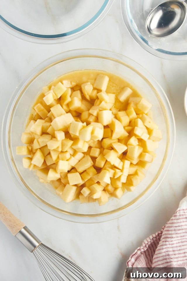 An overhead shot revealing a generous quantity of chopped apples meticulously folded into the cake batter within a large glass mixing bowl, ensuring even distribution for the French apple cake.