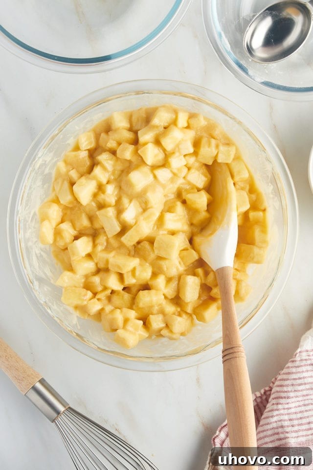A close-up, overhead view of the completed French apple cake batter, brimming with coated apple chunks, perfectly mixed in a glass bowl and ready for baking.