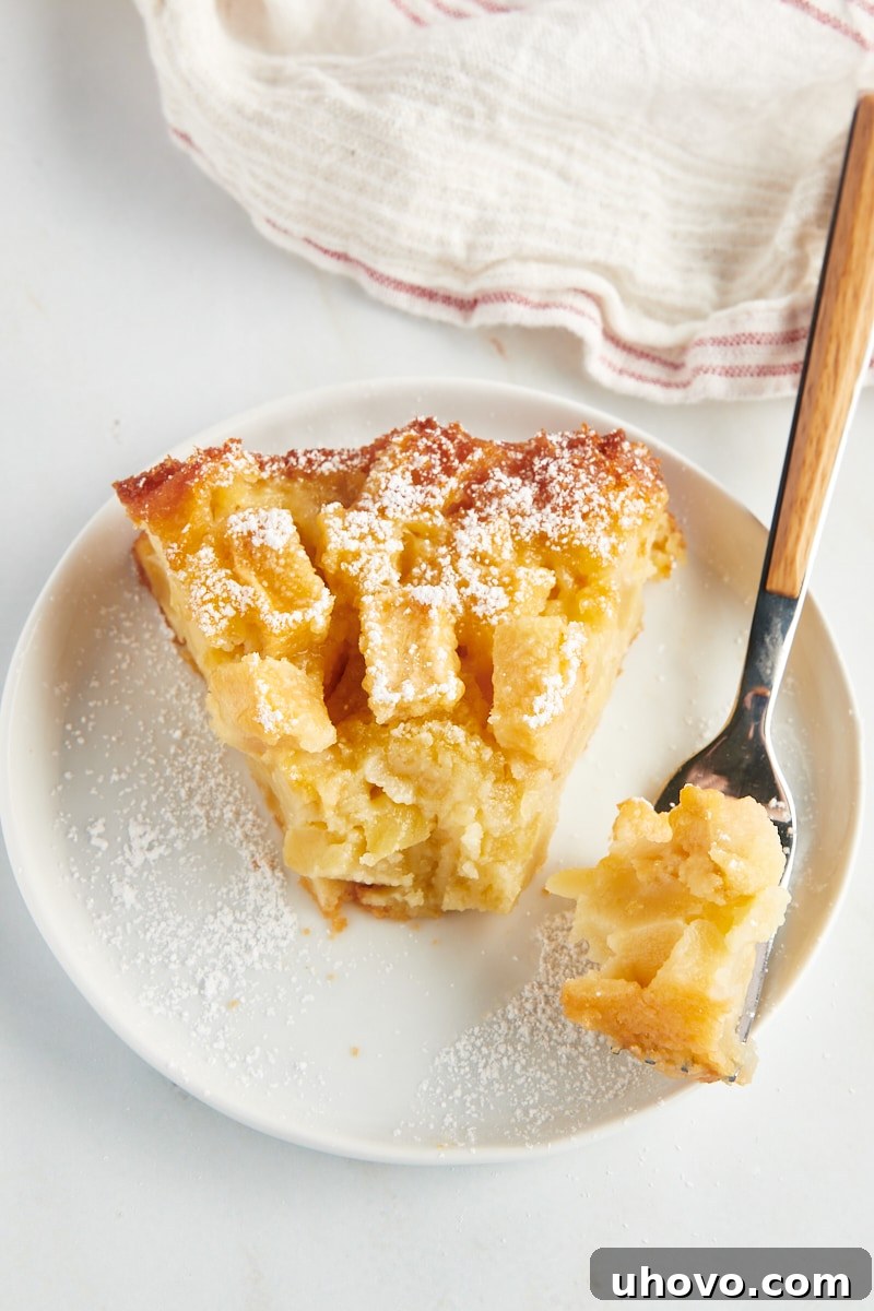 A tantalizing close-up of a slice of French apple cake, perfectly presented on a white plate, with a fork holding a bite-sized piece of cake, inviting you to savor its tender texture and rich flavor.