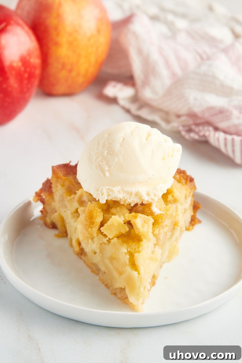 A charming slice of French apple cake generously adorned with a scoop of creamy vanilla ice cream, creating a delightful contrast of warm and cold textures.