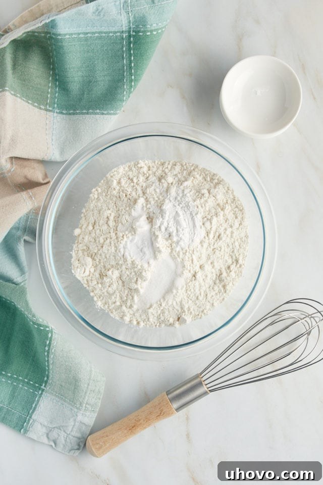 An overhead view of essential dry ingredients—cake flour, baking powder, baking soda, and salt—carefully measured into a clear glass mixing bowl, ready to be combined for the Louisiana Crunch Cake.