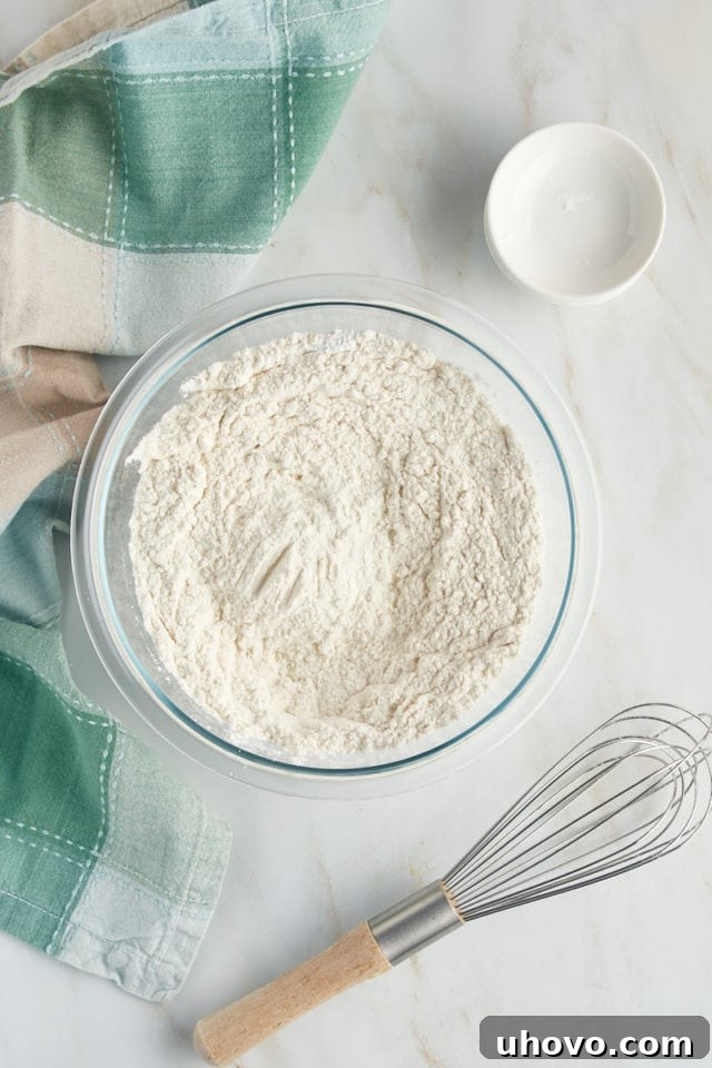 An overhead view of the thoroughly mixed dry ingredients for the Louisiana Crunch Cake, showcasing the uniform blend of flour, leavening agents, and salt in a glass mixing bowl.