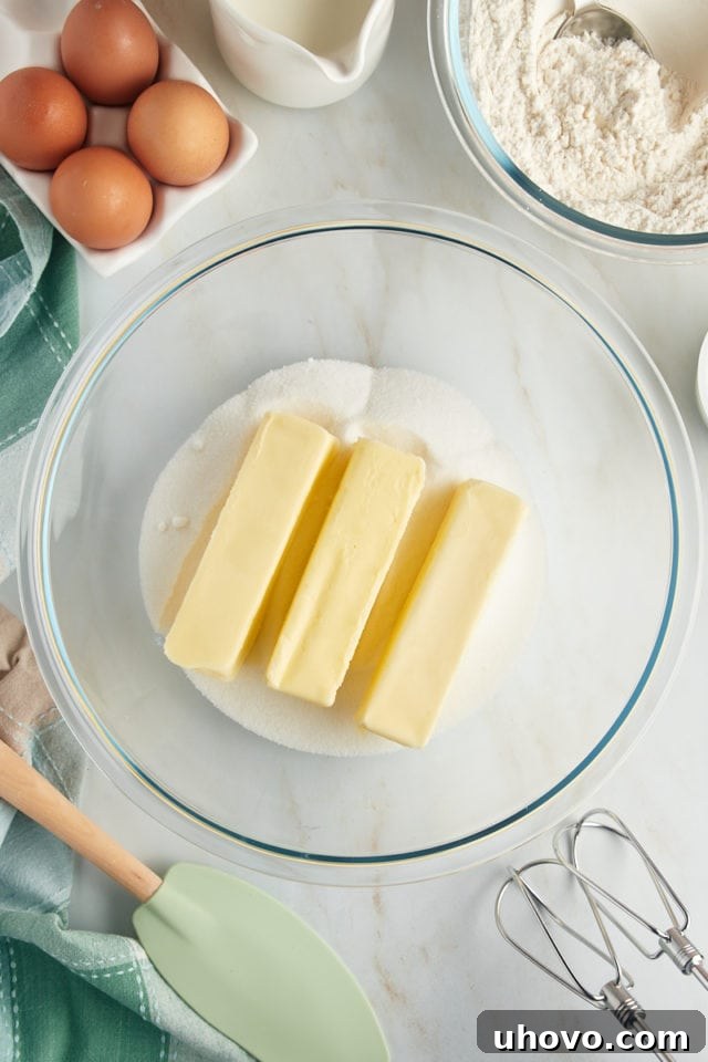 An overhead view of softened butter and granulated sugar combined in a clear glass mixing bowl, poised for the creaming process to create a fluffy cake batter base.
