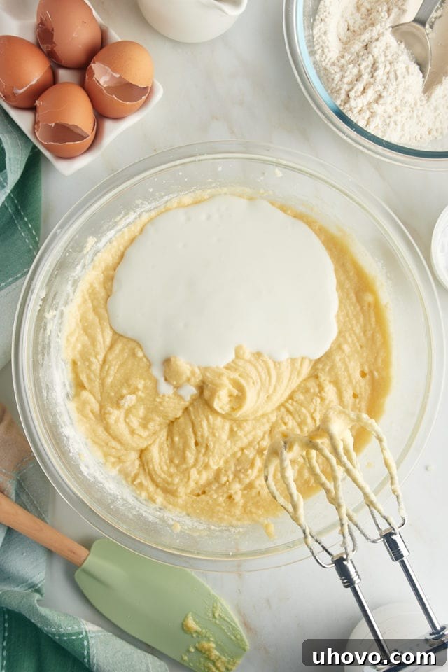 An overhead view showing buttermilk being added to the cake batter in a glass mixing bowl, contributing to the cake's moisture and tender crumb.
