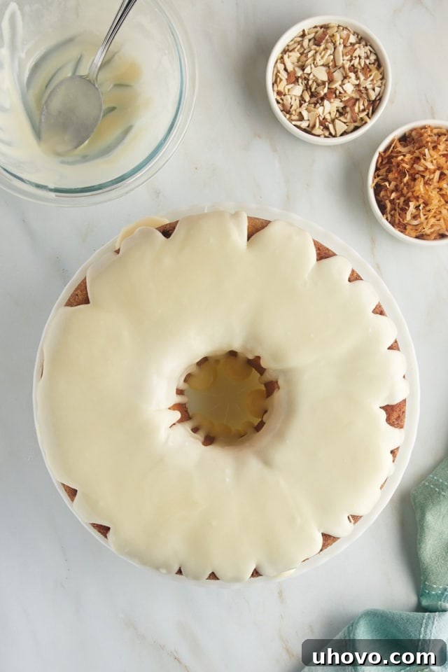 An overhead view of the Louisiana Crunch Cake on a white cake plate, now glistening with a generous pour of the sweet glaze, which cascades down its sides beautifully.