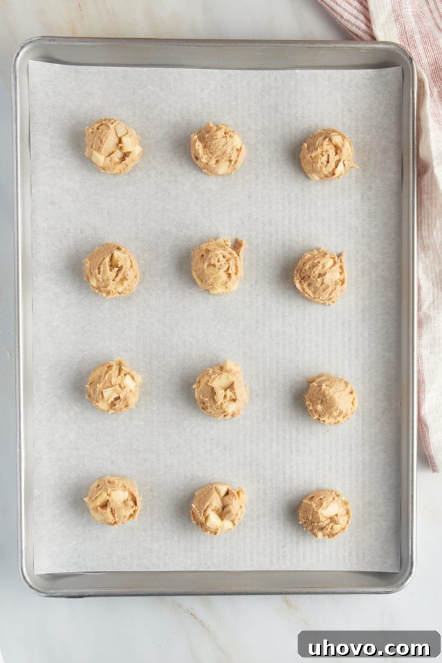 Overhead view of portioned apple cookie dough on a parchment-lined baking sheet.