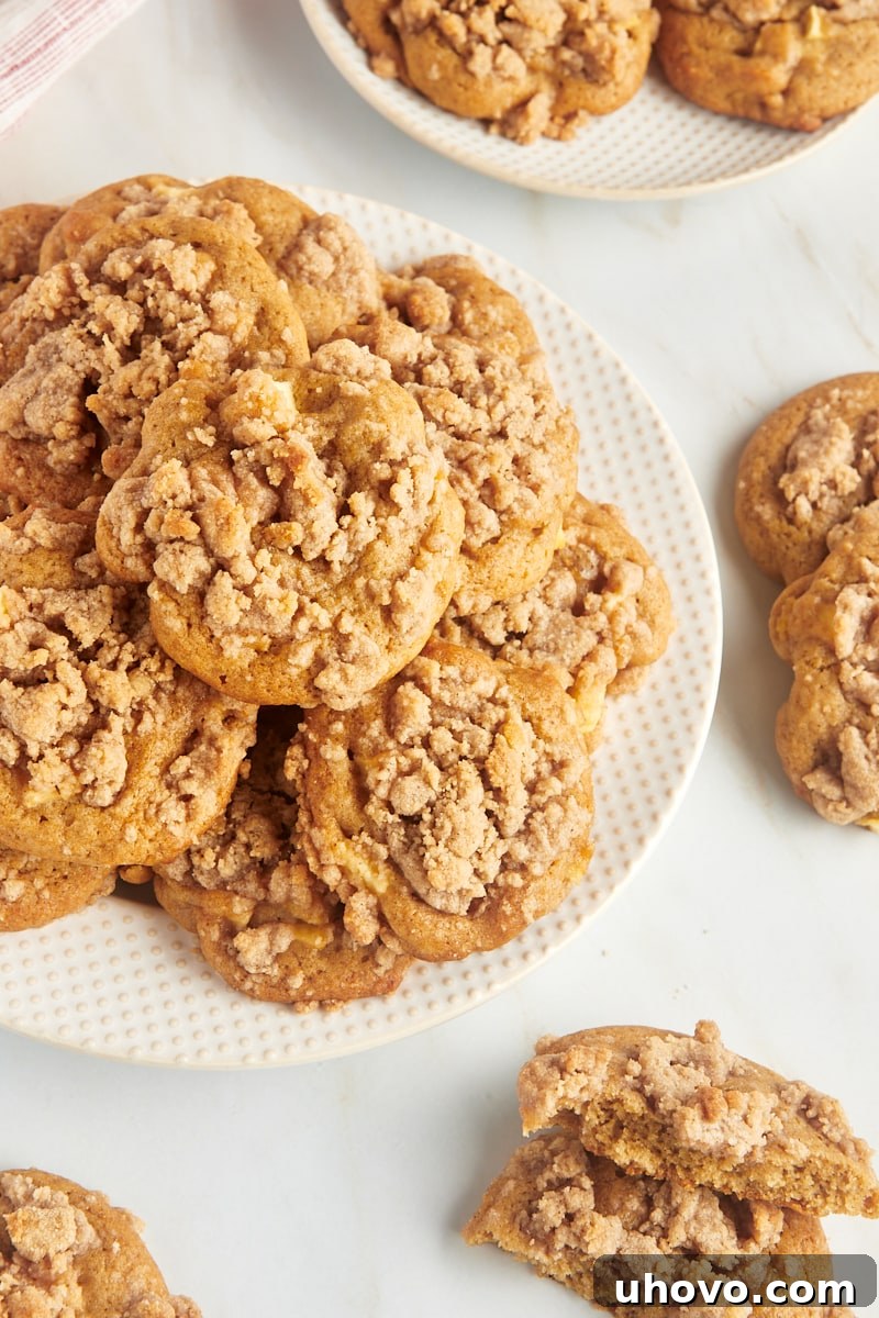 Crumb-topped apple cookies piled on a plate and scattered on a marble countertop.