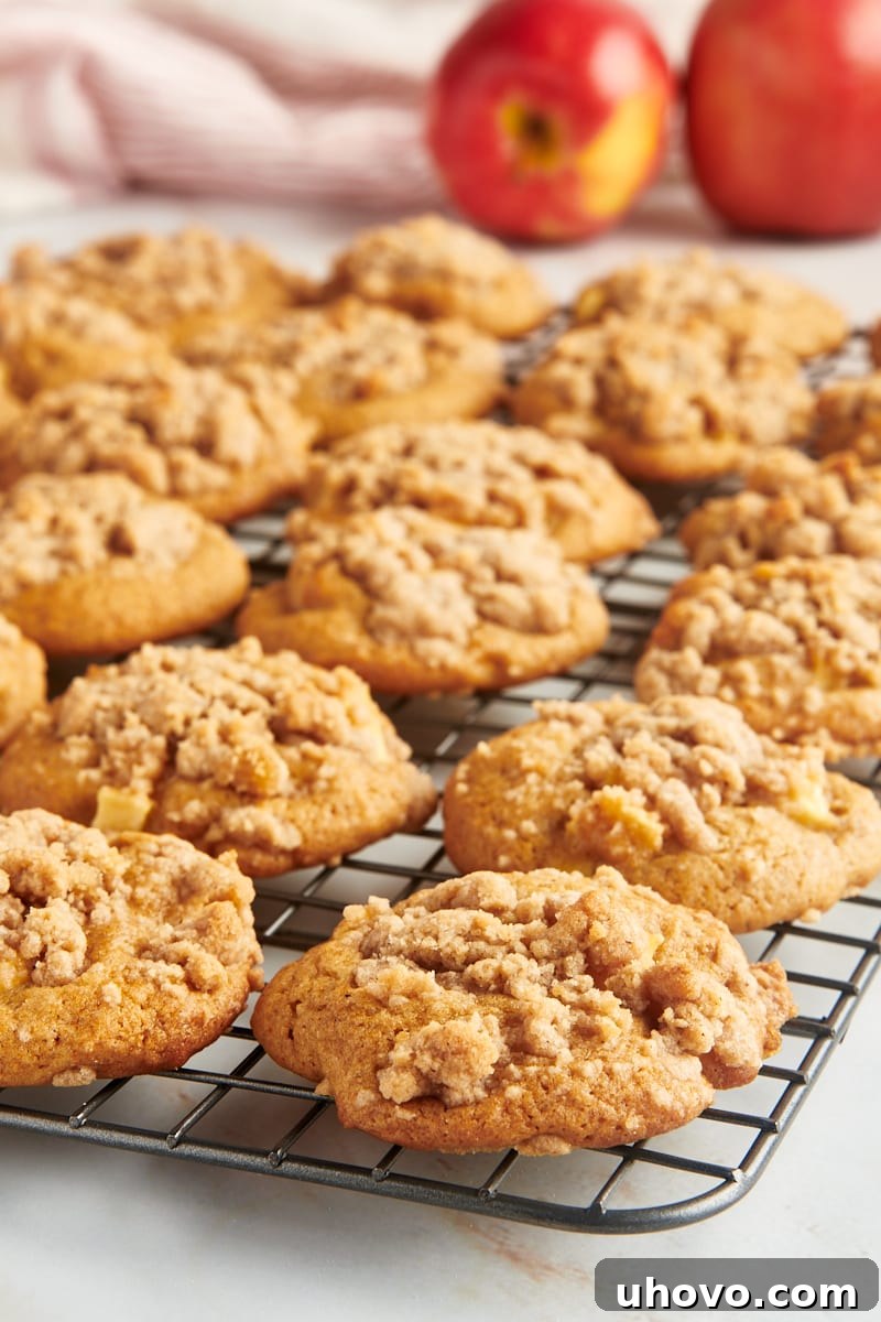 Crumb-topped apple cookies on a wire rack with two apples in the background.