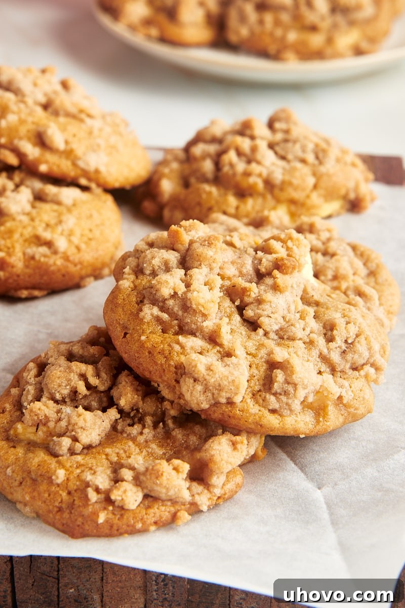 Two overlapping crumb-topped apple cookies on parchment paper with more cookies behind them.