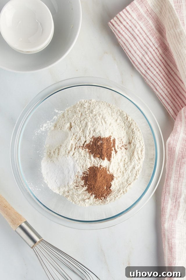 Overhead view of flour, cinnamon, nutmeg, baking soda, and salt in a glass mixing bowl.