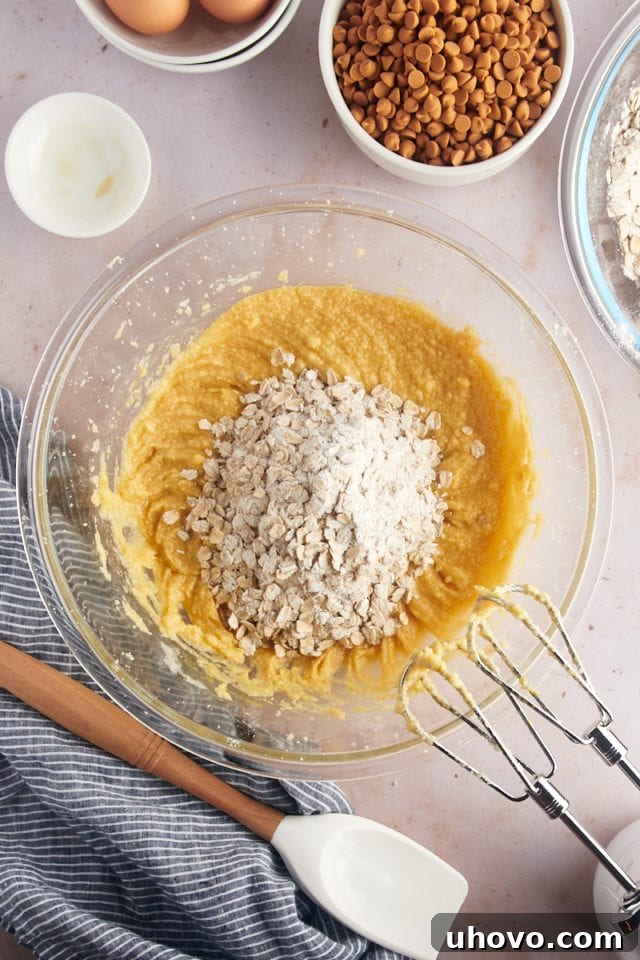 Overhead view of dry cookie ingredients added to wet ingredients in glass mixing bowl