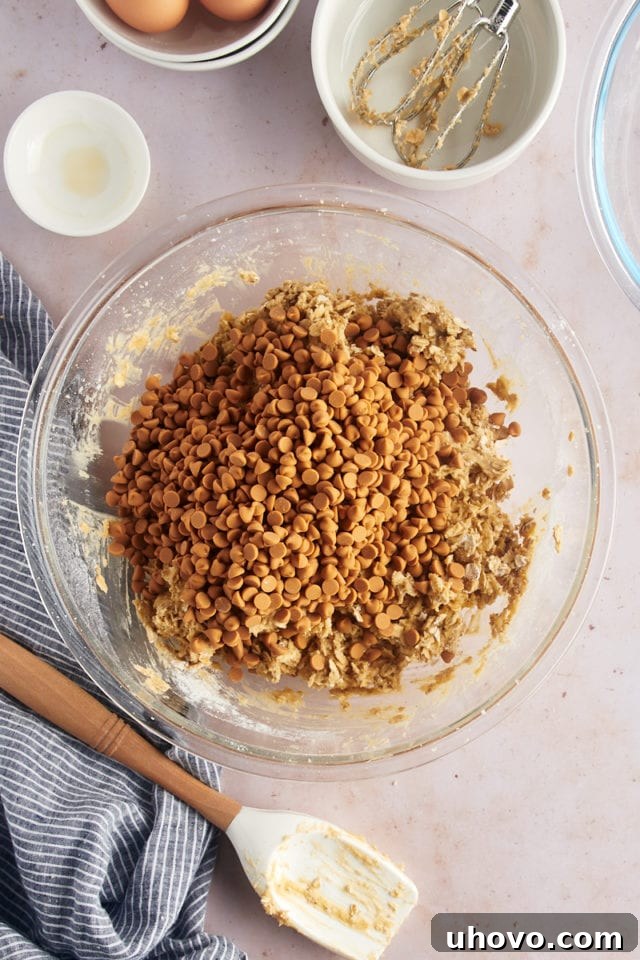 Overhead view of butterscotch chips added to bowl of cookie dough