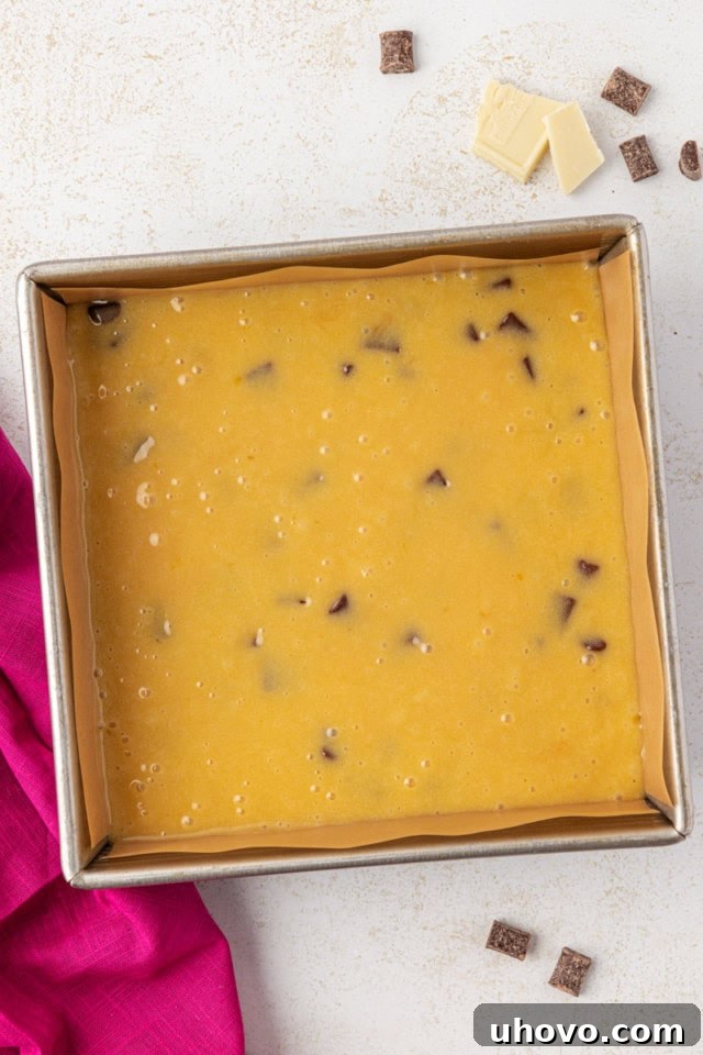 An overhead view of the complete white chocolate brownie batter evenly spread into an 8-inch square baking pan, ready to be placed in the oven.