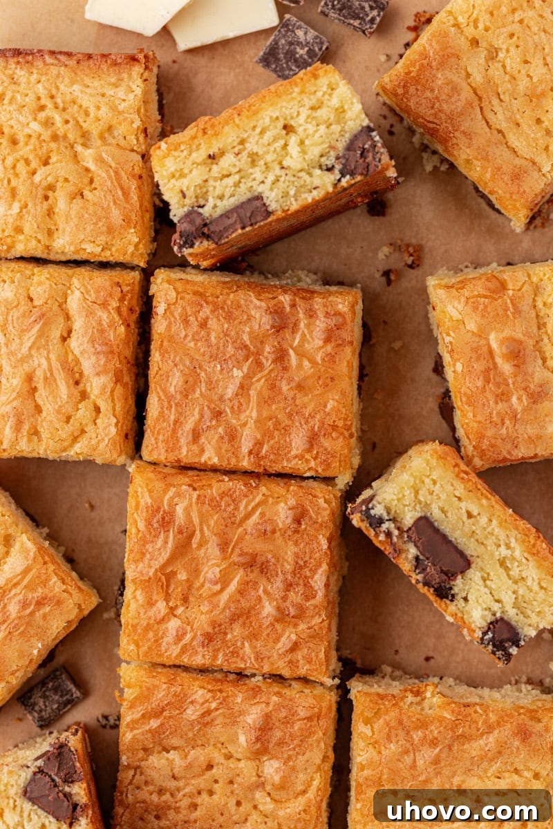 An overhead view of neatly sliced white chocolate brownies arranged on parchment paper, showcasing their dense, chewy texture and visible chocolate chunks.