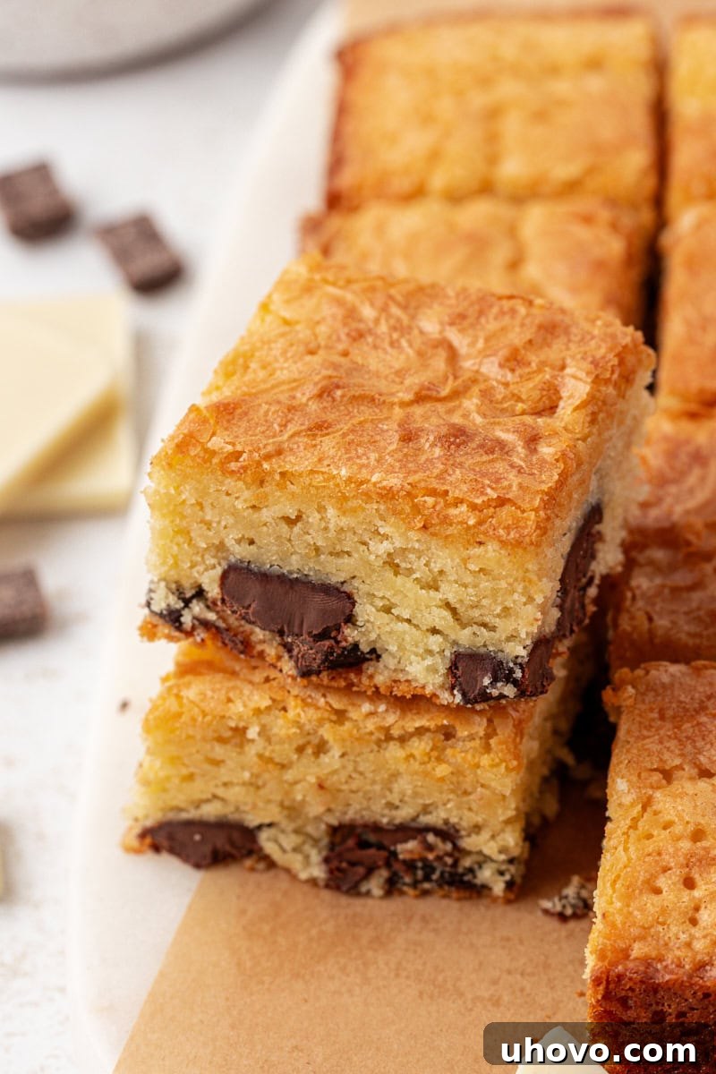 A perfectly stacked pair of white chocolate brownies, showcasing their thick, fudgy texture and appealing golden crust, with more brownies subtly blurred in the background.