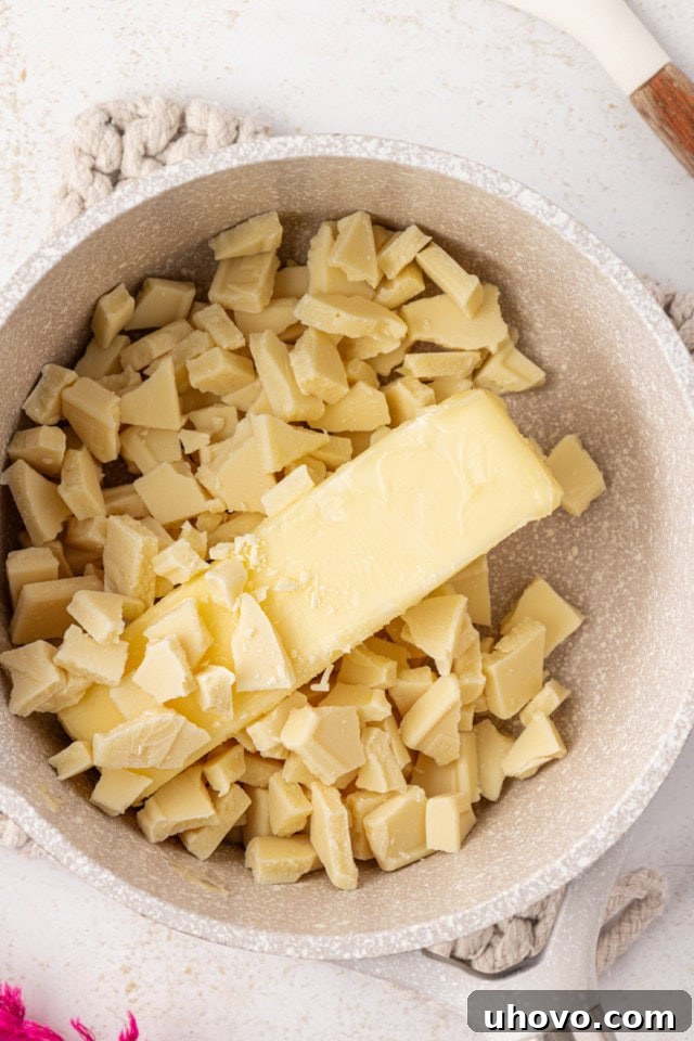 An overhead view of white chocolate pieces and butter cubes starting to melt in a saucepan over gentle heat.