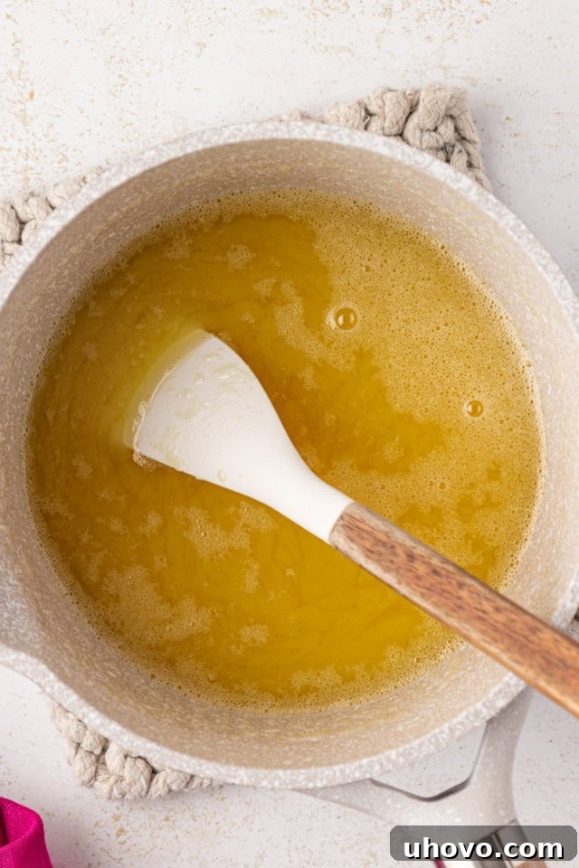 An overhead view of the smoothly melted white chocolate and butter mixture in a saucepan, glistening and ready to be cooled slightly.