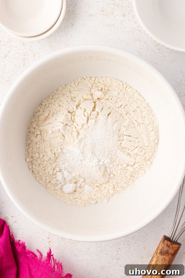 An overhead view of a white mixing bowl containing all-purpose flour, baking powder, and a pinch of salt, pre-mixed for the brownie batter.