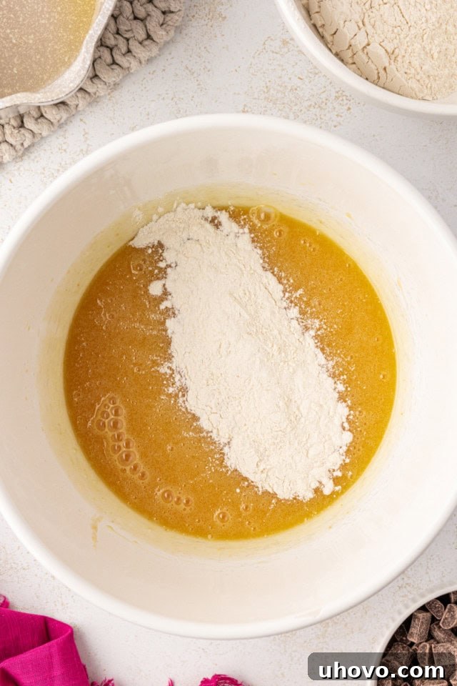 An overhead view of the dry ingredients (flour mixture) being gradually added to the wet ingredients in a white mixing bowl, ready for gentle mixing.