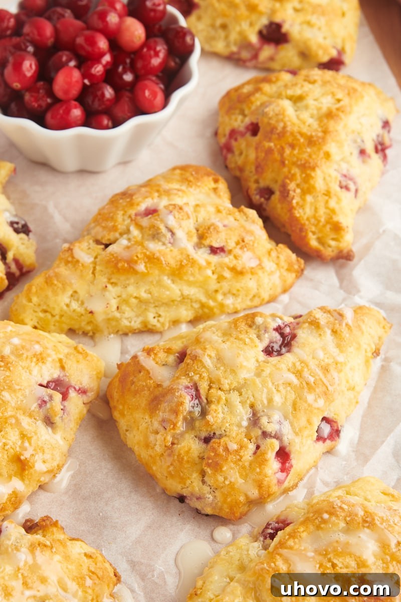 glazed cranberry orange scones on parchment paper alongside a small bowl of cranberries