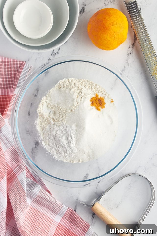 overhead view of flour, sugar, orange zest, baking powder, baking soda, and salt in a glass mixing bowl