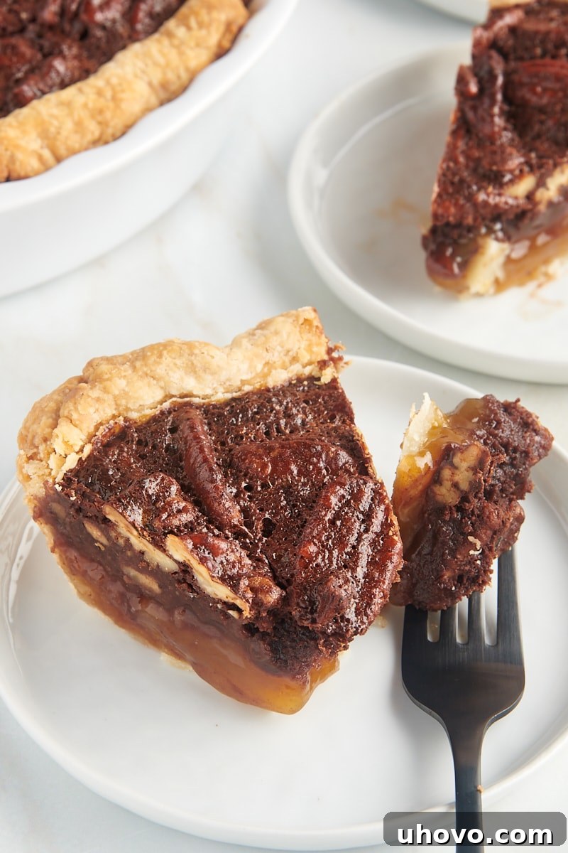 a slice of chocolate pecan pie on a white plate with a bite of pie on a fork
