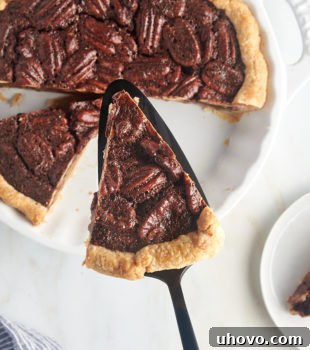 overhead view of a slice of chocolate pecan pie on a pie server over the remaining pie